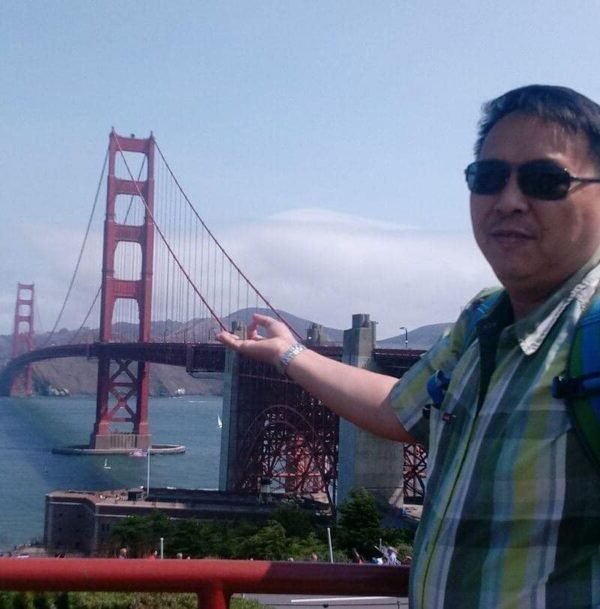 "Exporian member in a checkered shirt and sunglasses, gesturing towards the iconic Golden Gate Bridge in San Francisco."