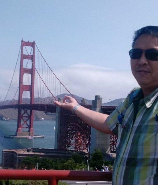 "Exporian member in a checkered shirt and sunglasses, gesturing towards the iconic Golden Gate Bridge in San Francisco."